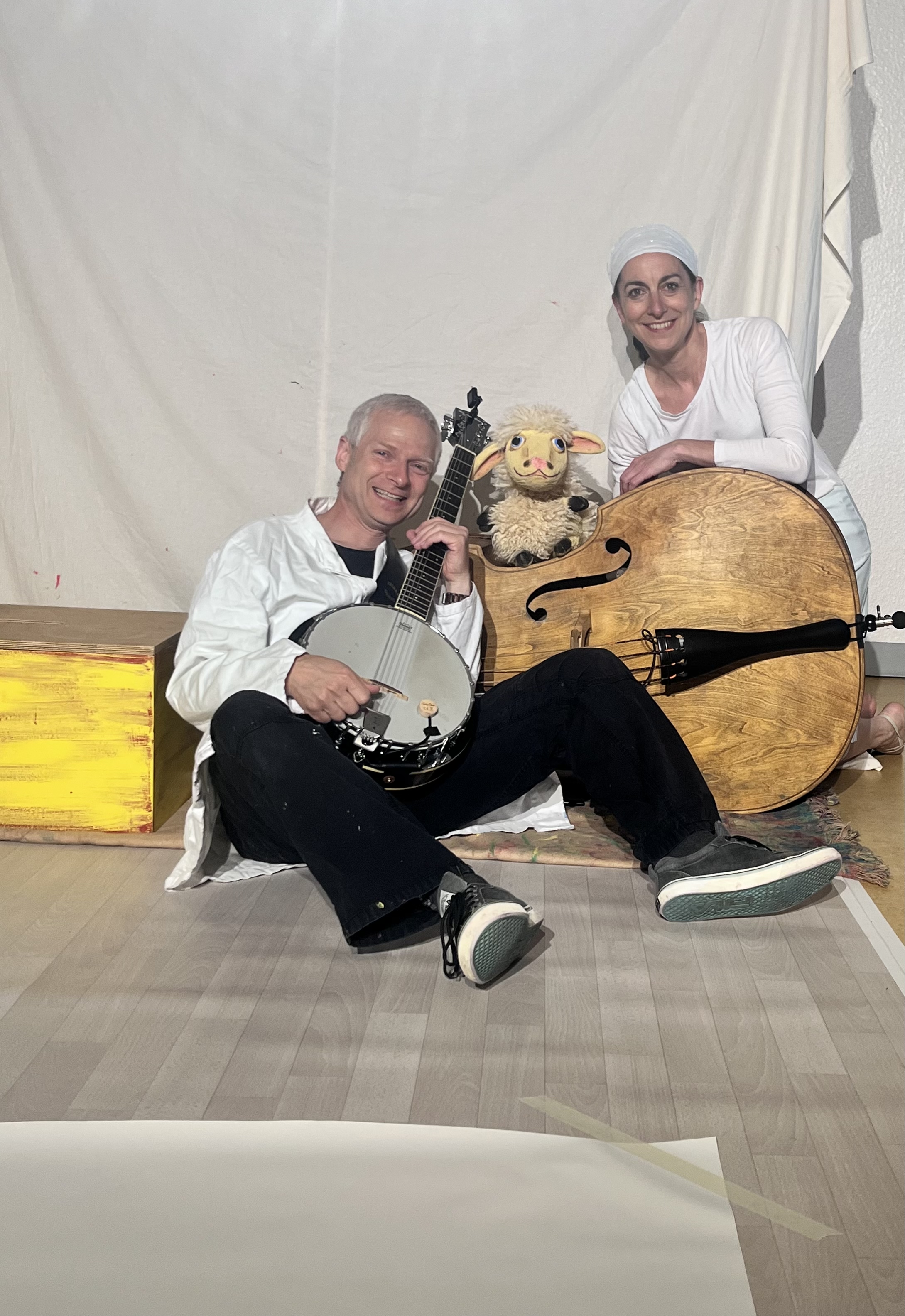 ein liegender Kontrabass, davor ein Mann mit Banjo, dahinter eine Frau mit Schafpuppe Lotta